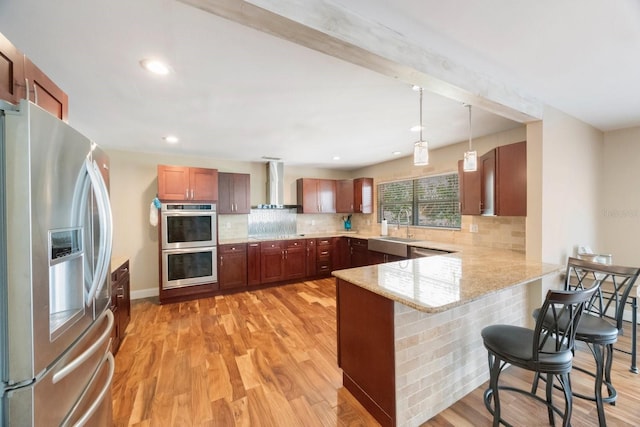 kitchen featuring light wood-type flooring, pendant lighting, stainless steel appliances, kitchen peninsula, and wall chimney exhaust hood