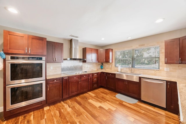 kitchen featuring a sink, backsplash, light wood finished floors, appliances with stainless steel finishes, and wall chimney range hood