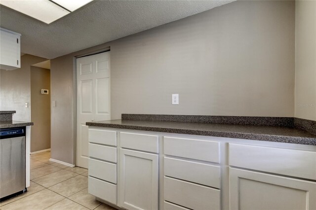 kitchen with white cabinets, dishwasher, light tile patterned floors, and a textured ceiling