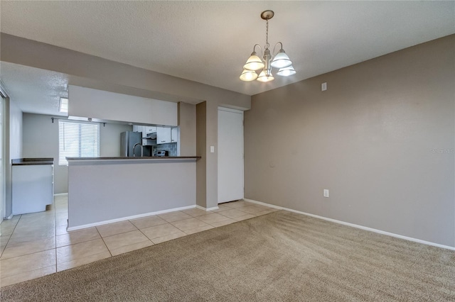 kitchen with stainless steel refrigerator, a textured ceiling, a chandelier, kitchen peninsula, and light colored carpet