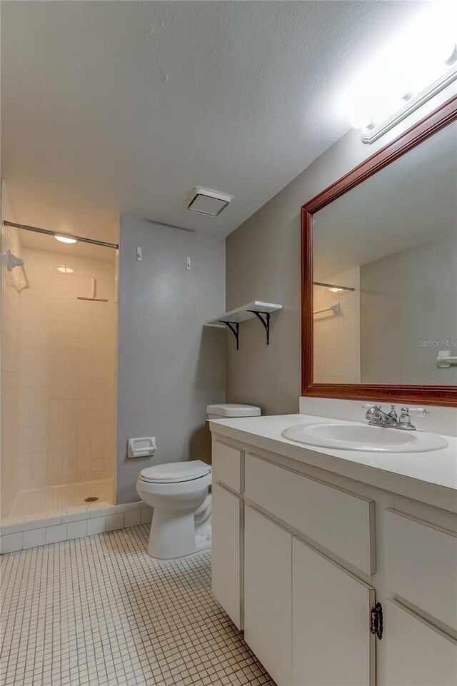 bathroom with tile patterned floors, toilet, a tile shower, vanity, and a textured ceiling