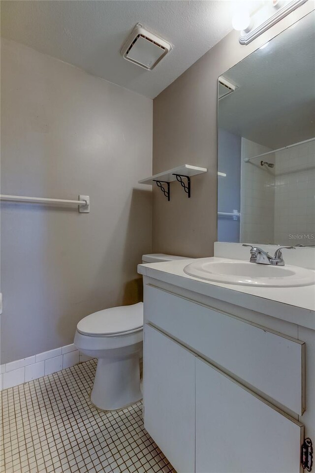 bathroom featuring a textured ceiling, vanity, toilet, tile patterned floors, and a shower