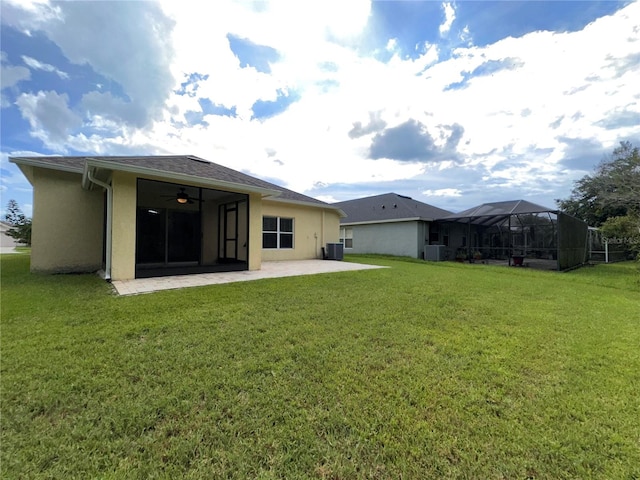 rear view of property with ceiling fan, a yard, a patio, a lanai, and central AC unit