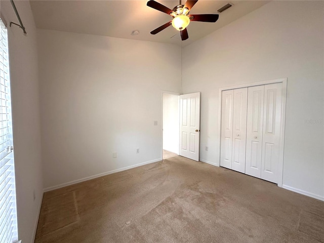 unfurnished bedroom featuring a towering ceiling, carpet floors, a closet, and ceiling fan