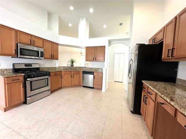 kitchen featuring recessed lighting, brown cabinets, appliances with stainless steel finishes, a towering ceiling, and a sink