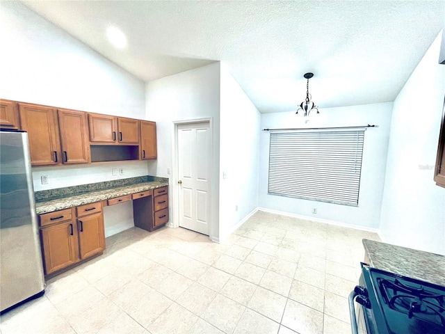 kitchen with brown cabinets, pendant lighting, range with gas stovetop, built in desk, and freestanding refrigerator