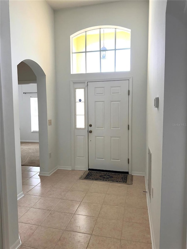 foyer with arched walkways, light tile patterned floors, baseboards, and a towering ceiling