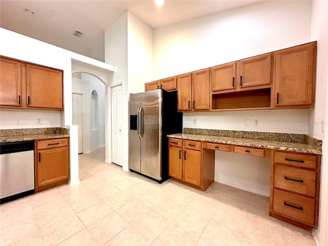 kitchen featuring a high ceiling, brown cabinetry, built in desk, and appliances with stainless steel finishes