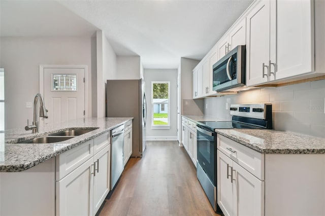 kitchen with light stone countertops, light hardwood / wood-style flooring, appliances with stainless steel finishes, sink, and white cabinets