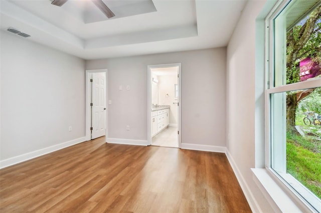 empty room with a healthy amount of sunlight, ceiling fan, light wood-type flooring, and a tray ceiling