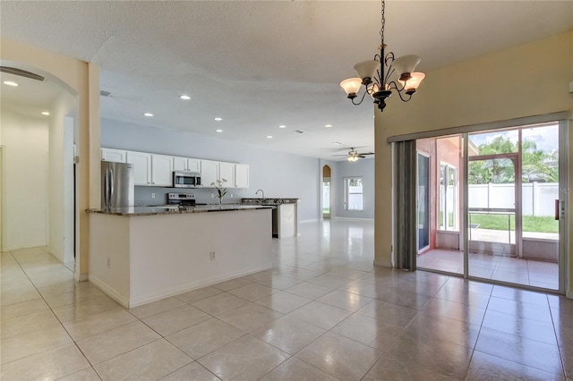 kitchen with white cabinets, pendant lighting, stainless steel appliances, dark stone countertops, and ceiling fan with notable chandelier