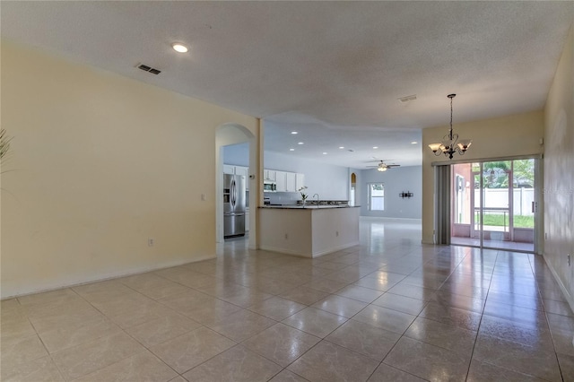 interior space with white cabinets, hanging light fixtures, light tile patterned floors, stainless steel fridge with ice dispenser, and ceiling fan with notable chandelier