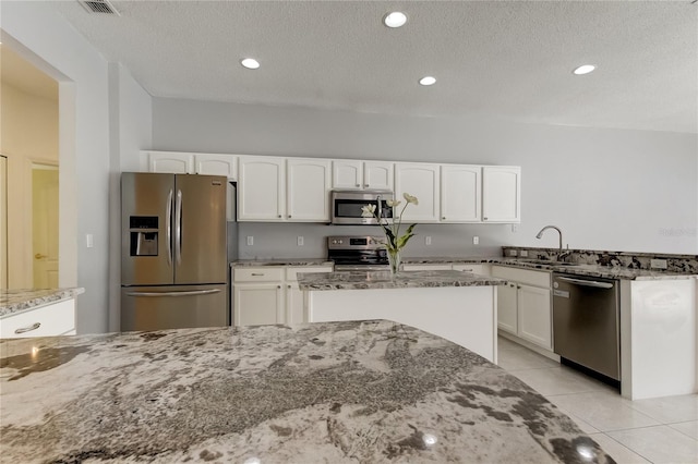 kitchen with white cabinets, light tile patterned floors, stainless steel appliances, stone counters, and sink