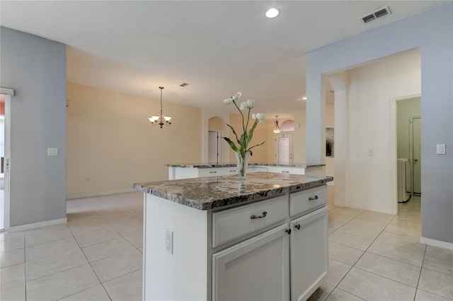 kitchen with dark stone countertops, light tile patterned flooring, white cabinets, pendant lighting, and a center island