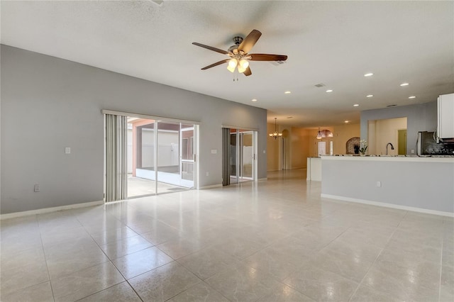 unfurnished living room with ceiling fan with notable chandelier, sink, and light tile patterned floors