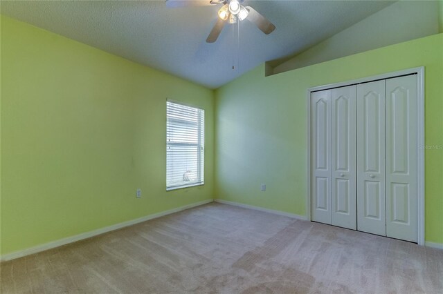 unfurnished bedroom with ceiling fan, a textured ceiling, a closet, light carpet, and vaulted ceiling