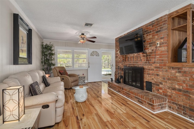 living room featuring a fireplace, light wood-type flooring, crown molding, and ceiling fan