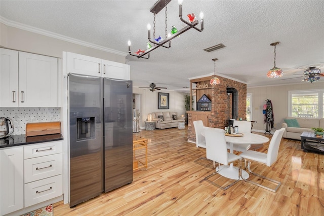 kitchen with light hardwood / wood-style flooring, decorative light fixtures, a wood stove, stainless steel fridge, and ceiling fan