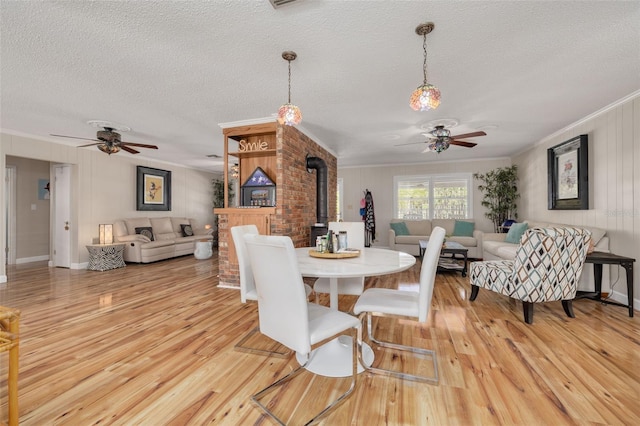 dining space with ornamental molding, light hardwood / wood-style flooring, ceiling fan, and a wood stove