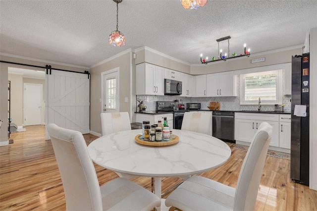 dining room with crown molding, a barn door, a notable chandelier, and light hardwood / wood-style floors