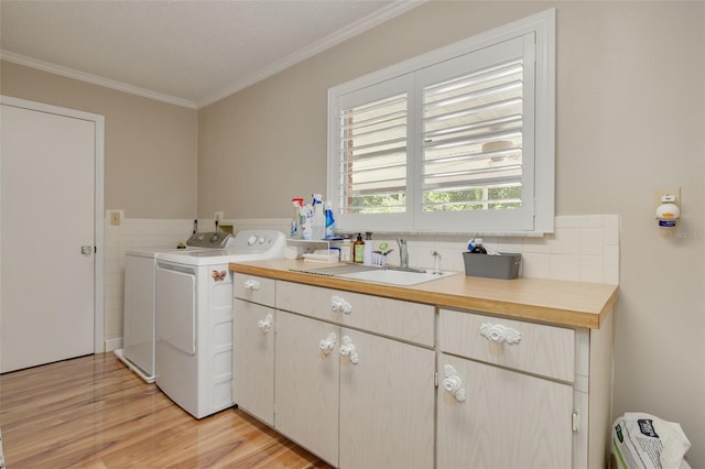 clothes washing area featuring cabinets, washer and clothes dryer, ornamental molding, light hardwood / wood-style flooring, and sink