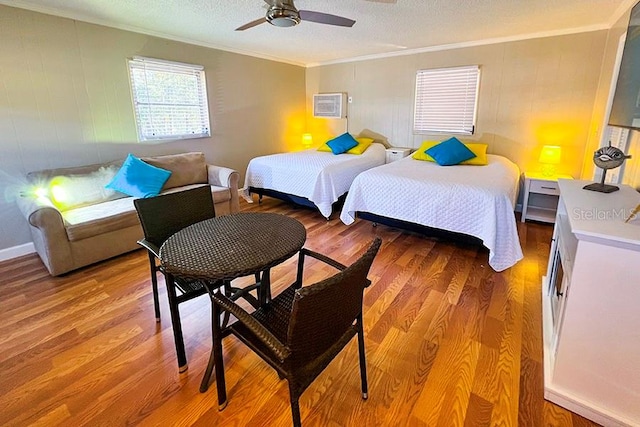 bedroom with ornamental molding, a wall mounted AC, a textured ceiling, ceiling fan, and hardwood / wood-style flooring