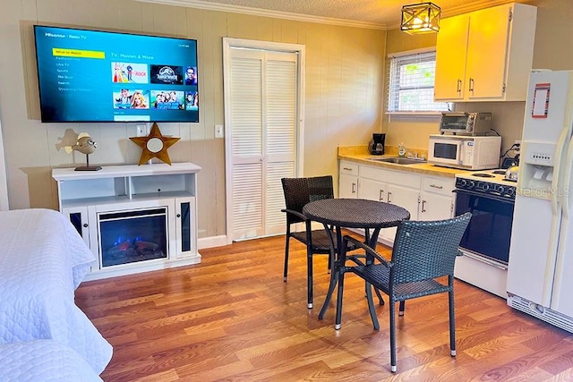 kitchen featuring light wood-type flooring, wooden walls, crown molding, white appliances, and sink