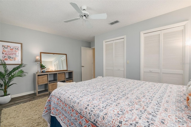 bedroom featuring dark wood-type flooring, ceiling fan, a textured ceiling, and multiple closets