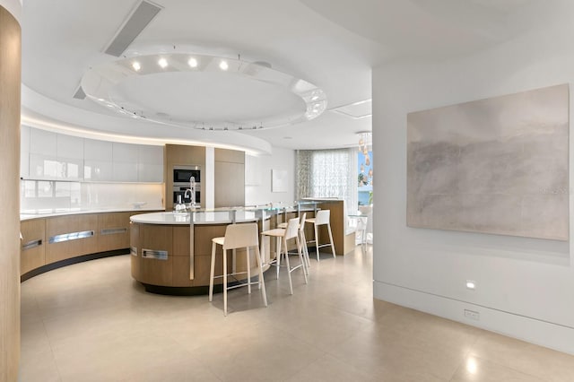 kitchen featuring a breakfast bar area, a large island with sink, a raised ceiling, and sink