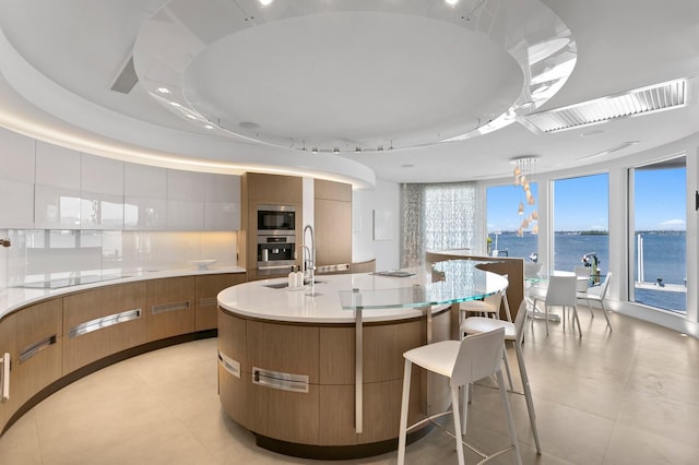 kitchen with a large island, a tray ceiling, stainless steel appliances, a water view, and decorative backsplash