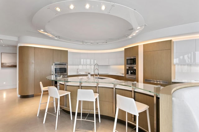 kitchen featuring a kitchen island with sink, stainless steel appliances, sink, and a breakfast bar