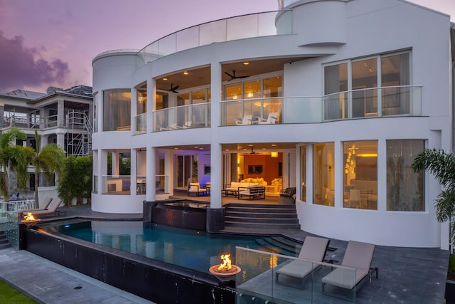 back house at dusk with a patio, a balcony, and an outdoor living space with a fire pit