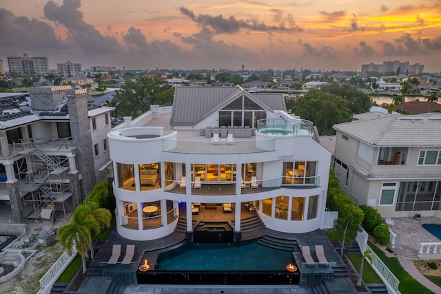 back house at dusk featuring a balcony and a fenced in pool