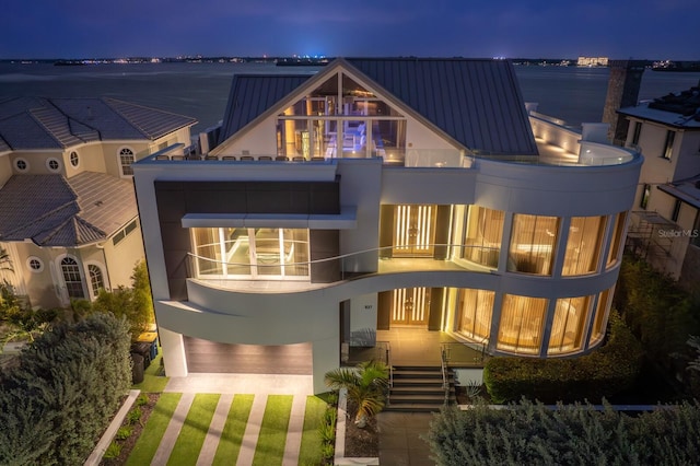 back house at night featuring a balcony and a water view