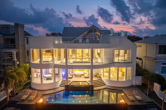 back house at dusk with a balcony and a patio area