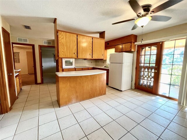 kitchen with ceiling fan, light tile patterned floors, a textured ceiling, a center island, and white appliances