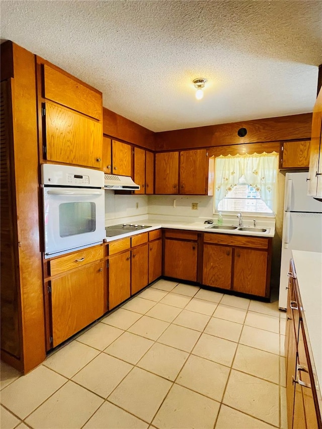 kitchen with sink, a textured ceiling, white appliances, and light tile patterned floors