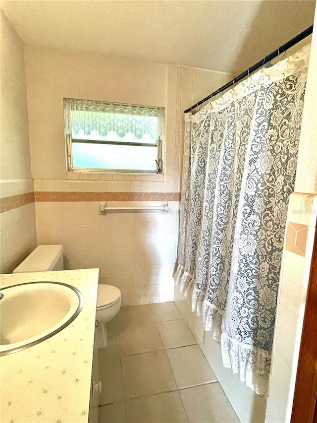 bathroom with a textured ceiling, tile walls, toilet, vanity, and tile patterned floors