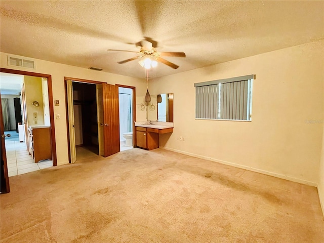 unfurnished bedroom featuring ensuite bathroom, sink, a textured ceiling, ceiling fan, and light colored carpet