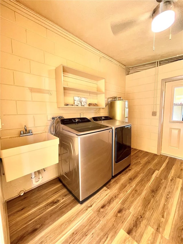 clothes washing area with sink, light wood-type flooring, independent washer and dryer, a textured ceiling, and water heater