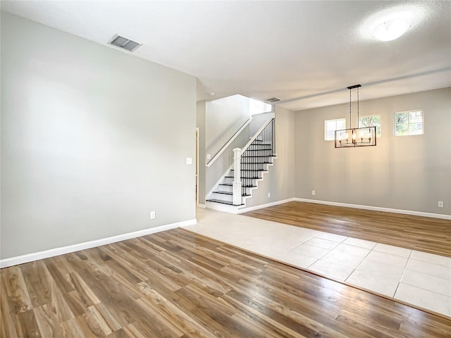 empty room featuring baseboards, visible vents, wood finished floors, stairs, and a notable chandelier