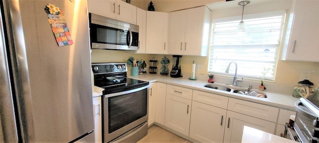 kitchen featuring pendant lighting, light tile floors, appliances with stainless steel finishes, white cabinetry, and sink