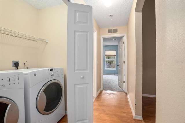 washroom with light hardwood / wood-style flooring, separate washer and dryer, a textured ceiling, and electric dryer hookup