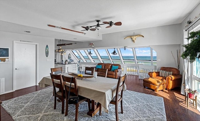 dining room with a water view, ceiling fan with notable chandelier, a healthy amount of sunlight, and dark wood-type flooring