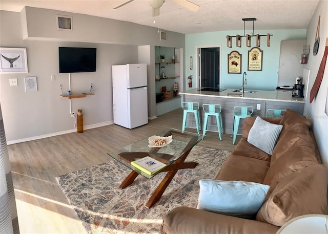 living room with a textured ceiling, ceiling fan, sink, and light hardwood / wood-style flooring