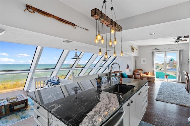 kitchen with ceiling fan, dark wood-type flooring, white cabinets, dark stone counters, and a center island with sink