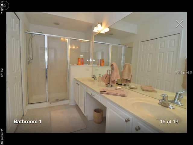 bathroom with an enclosed shower, dual sinks, vanity with extensive cabinet space, and tile flooring