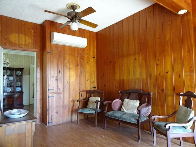 sitting room featuring wooden walls, a wall mounted AC, ceiling fan, dark hardwood / wood-style flooring, and a textured ceiling