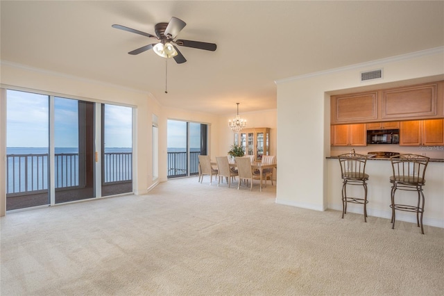 unfurnished living room with light colored carpet, ceiling fan with notable chandelier, a water view, and ornamental molding