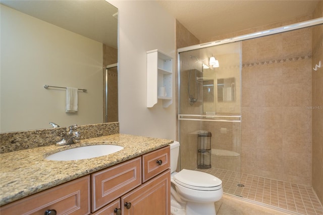 bathroom featuring tile patterned flooring, vanity, a shower with shower door, and toilet